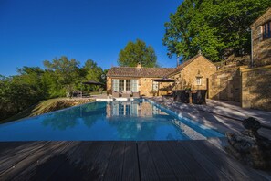 Una casa de piedra con piscina, mobiliario de exterior y terraza de madera.