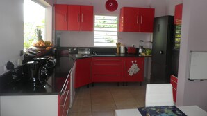 Una cocina con armarios rojos, un refrigerador negro y una ventana con persianas.