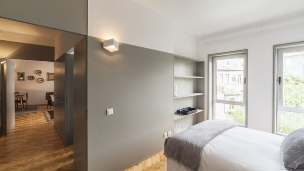 A modern bedroom with a bed, built-in shelves, and a view of the outside. - CdC II Apartments By Tale House (Porto)