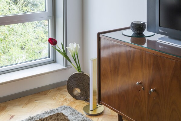 A room with a wooden cabinet, a glass table, a vase with flowers, and a television.
