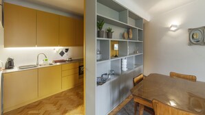 A compact kitchen with modern appliances, a dining area with a wooden table and chairs, and a built-in shelving unit with decorative items. - CdC II Apartments By Tale House (Porto)