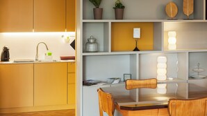 A modern kitchen with a built-in stove, a sink, and a coffee maker. There is a dining table with chairs and a shelf with decorative items. - CdC II Apartments By Tale House (Porto)