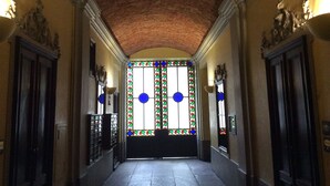Corredor com teto de tijolos, portas ornamentadas e vitrais.