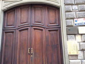 A large wooden double door with brass handles, set within a stone wall with a number plaque and a sign for a business. - Alle Volte Turin - historic center (TORINO)