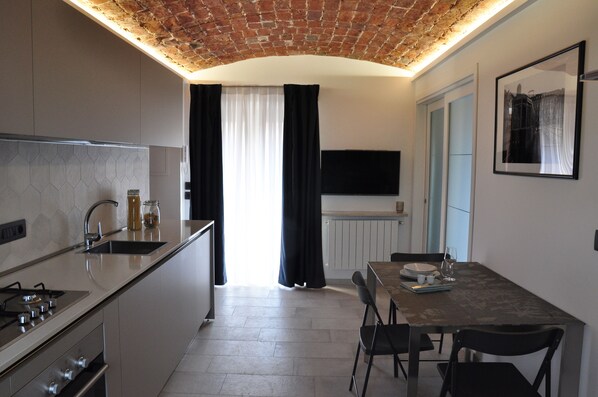A modern kitchen with a built-in stove, a sink, and a dining area with a table and chairs. - Alle Volte Turin - historic center (TORINO)