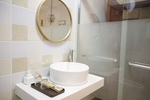 A bathroom with a round white sink, a mirror, and a glass shower door. - Mingrentang Inn (Nanjing)