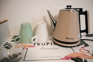 A kitchen area with a coffee maker, a kettle, and a mug on a table with a floral tablecloth. - Mingrentang Inn (Nanjing)