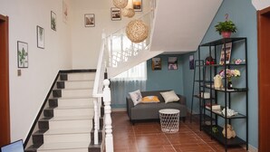 Eine Treppe mit weißen Geländern führt zu einem Wohnbereich mit einem grauen Sofa, einem weißen runden Tisch und einem schwarzen Bücherregal mit Dekorationselementen.