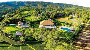 An aerial view of a resort with multiple buildings, including a large central structure with a tiled roof, surrounded by lush greenery and terraced fields. - Exclusive 5 star villa with 365 ° view of the sea, mountains and rice fields! (Kayu Putih)