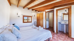 Ein Schlafzimmer mit einem großen Bett, Holzbalken, einem Badezimmer mit Waschbecken und Spiegel sowie Blick ins Freie.