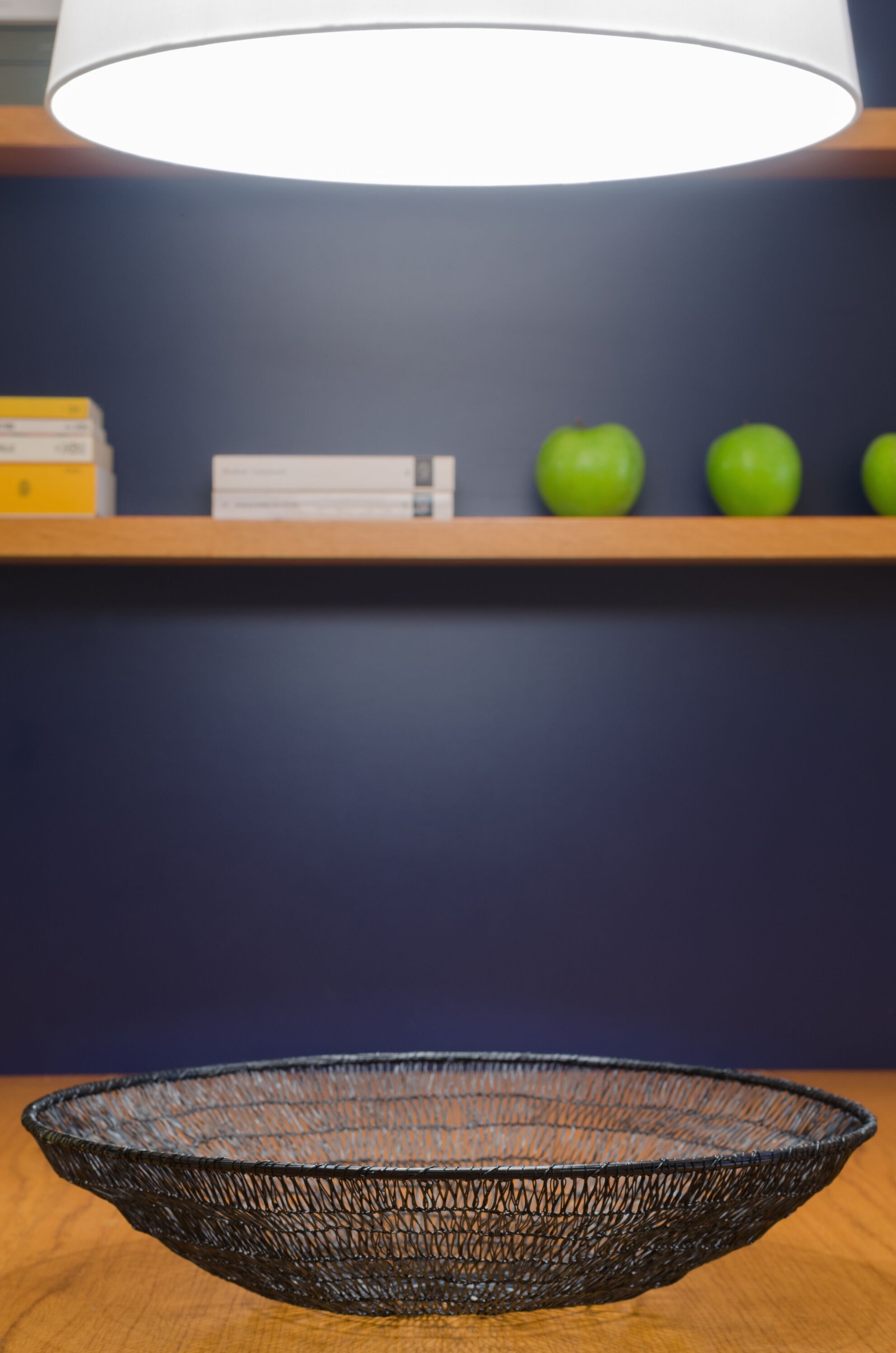 Un panier en fil de fer posé sur une table en bois, avec une lampe au-dessus.