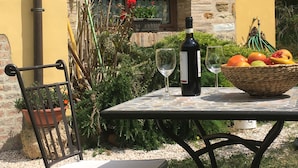 A table with a bottle of wine, two glasses, and a fruit bowl. - Country Cottage / Gite - Pergola (Pergola)