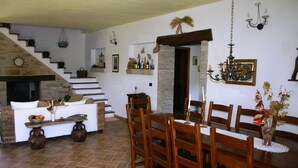 A dining area with wooden chairs and a table, a staircase with a stone wall, and a chandelier. - Country Cottage / Gite - Pergola (Pergola)
