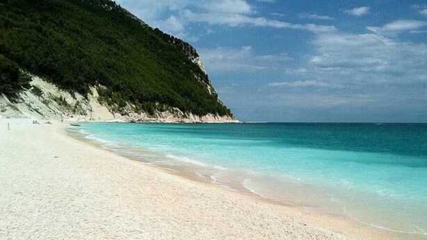 A beach with white sand and clear turquoise water, bordered by a forested cliff. - Country Cottage / Gite - Pergola (Pergola)