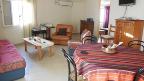 Un salon comprenant un canapé, une table à manger avec des chaises, un meuble en bois et un téléviseur fixé au mur.