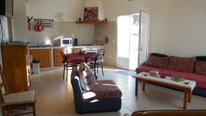 Un grand espace de vie comprenant un canapé, une table basse et une table à manger avec des chaises. Il y a également un coin cuisine équipé d’un four à micro-ondes et d’une cuisinière.