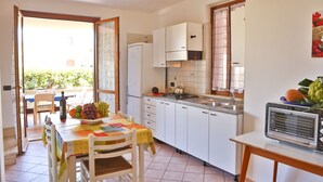 A compact kitchen with white cabinets, a tiled backsplash, and a small dining area with a table set for two. - WELL-LIT MEDITERRANEAN VILLA WITH VERANDA AND GARDEN ONLY 50 METERS FROM THE SEA (Campofelice PA, Italia)