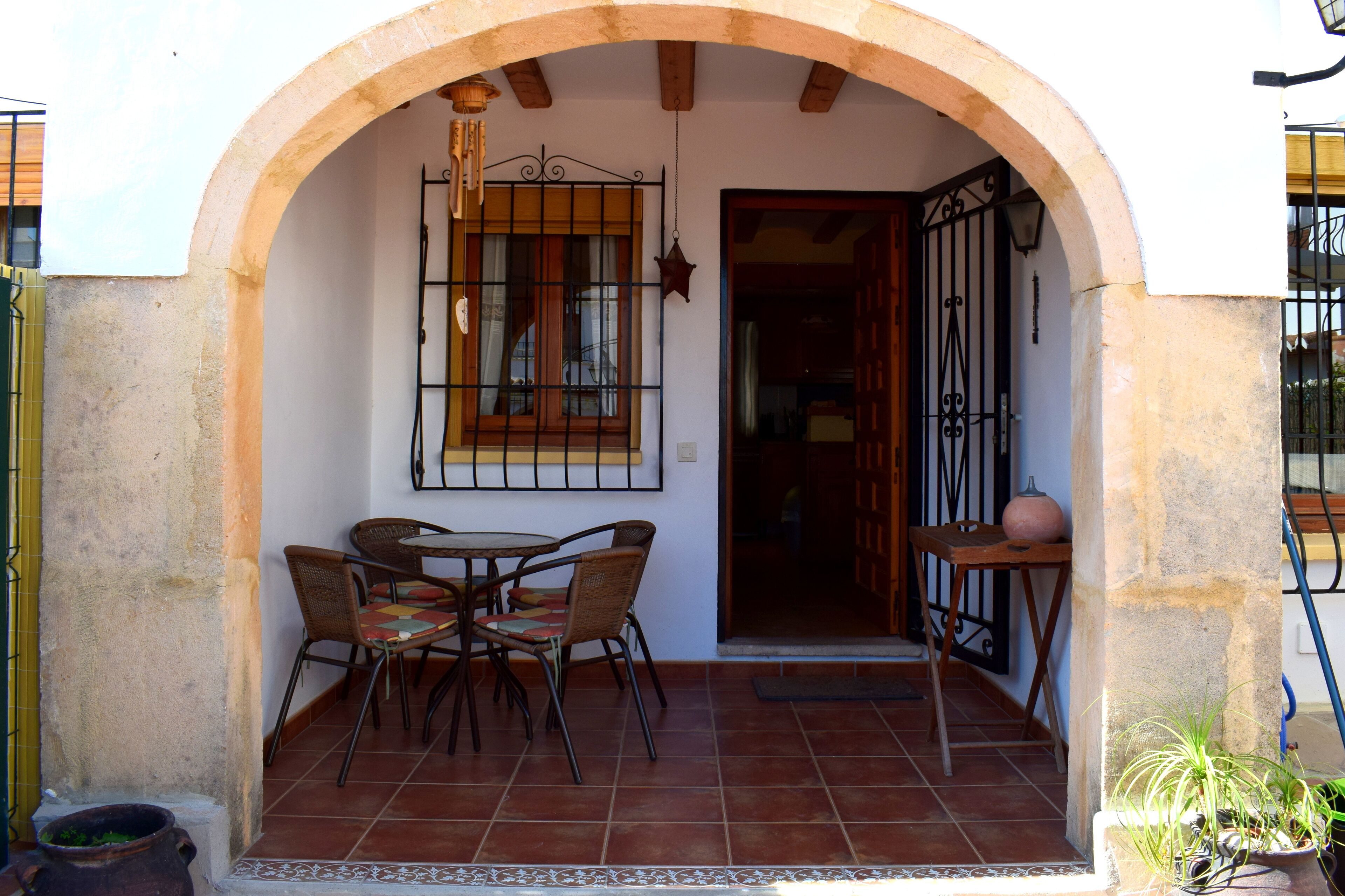 A patio with a table and chairs, an archway, a window with bars, and a door.