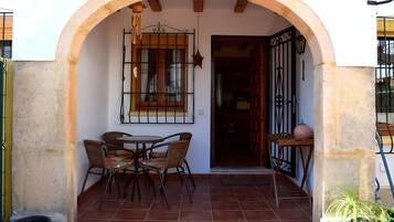 A patio with a table and chairs, an archway, a window with bars, and a door.