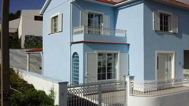Un bâtiment à deux étages, avec des volets blancs, un balcon et une clôture en métal.