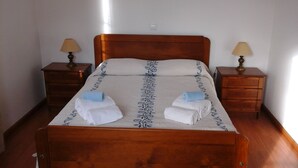 Un lit bien fait, avec une tête de lit en bois, deux tables de chevet avec des lampes et une petite commode en bois.