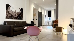 Un salon spacieux agrémenté d’un lustre moderne, d’un canapé en cuir noir, d’un fauteuil à bascule rose et d’un coin repas avec une table et des chaises.