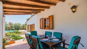 Un coin repas avec une table en bois dressée pour quatre personnes, entourée de chaises dotées de coussins turquoise, le tout sous un plafond avec des poutres en bois.