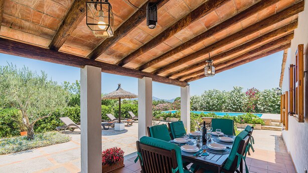Une terrasse extérieure dotée d’une pergola en bois, d’une table à manger pour quatre personnes et offrant une vue sur une piscine et un jardin.