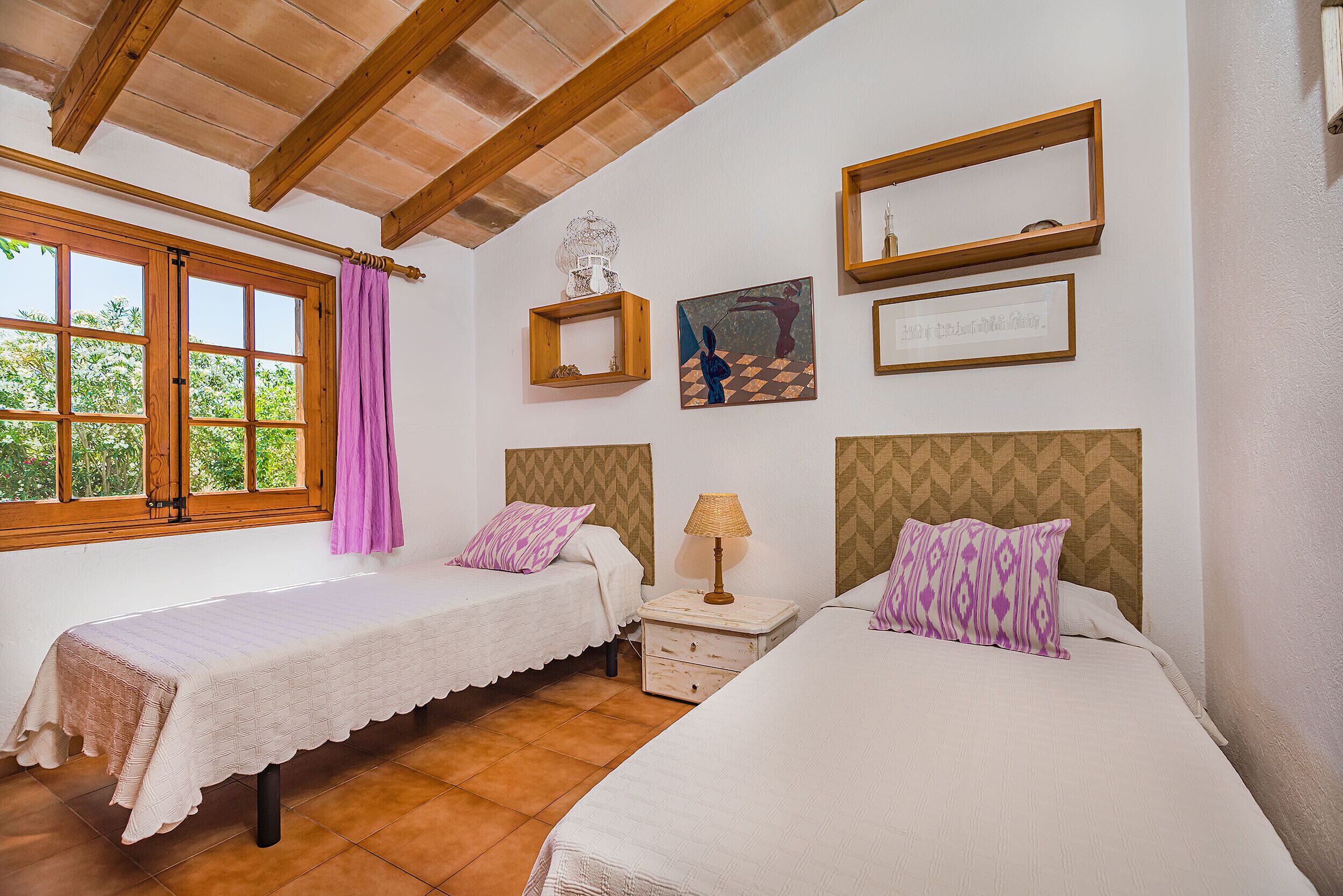 Una habitación con dos camas, una ventana con cortinas y obras de arte en las paredes.