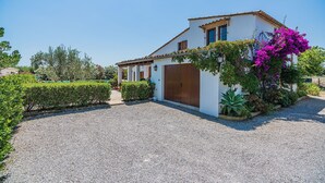 Un bâtiment blanc avec une porte marron, entouré de gravier et de verdure.