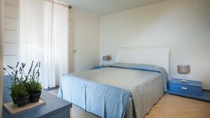Quarto com cama, mesas de cabeceira, abajur e planta.