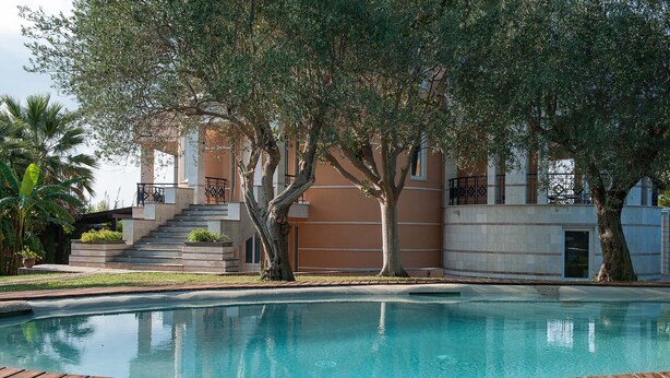 Piscina com deck de madeira, rodeada por árvores e um edifício com escadas.