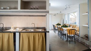 Uma cozinha moderna com ilha integrada, área de jantar com mesa comprida e cadeiras, e vista para o exterior através de grandes janelas.
