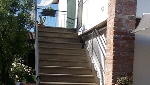 A set of outdoor stone steps leading up to a building with a white exterior and a brick column. There are potted plants on the steps and along the building's exterior. - Casale Gelsomino First floor (ROVOLON)