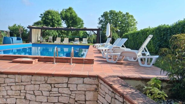 A swimming pool with a stone wall, lounge chairs, and a pergola. - Casale Gelsomino First floor (ROVOLON)