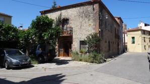 Un bâtiment en pierre de deux étages, doté d’un balcon, avec des voitures garées devant et un ciel dégagé.
