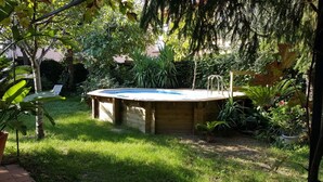 Un bain à remous en bois, situé dans un jardin entouré de verdure, avec une chaise à proximité.