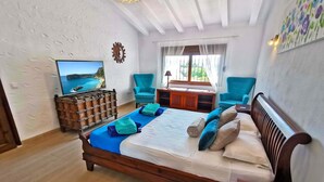 A bedroom with a wooden bed, a TV on the wall, and two chairs. - Lovely villa, near town, huge 76m2 pool, see the video ! (Javea)