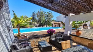 A covered outdoor seating area with wicker furniture, a pool in the background, and a view of a house and trees. - Lovely villa, near town, huge 76m2 pool, see the video ! (Javea)