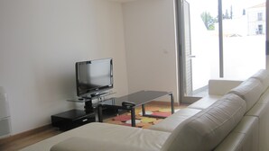 A living room with a flat-screen TV on a glass table, a white sofa, and a colorful rug. - Duplex apartment in the center of town with swimming pool, 3 bedrooms, for 6 (tavira)