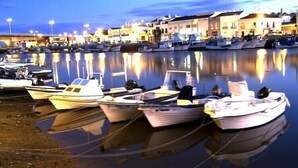 A marina with several boats docked, a calm water surface reflecting the boats and buildings, and a row of buildings along the waterfront. - Duplex apartment in the center of town with swimming pool, 3 bedrooms, for 6 (tavira)