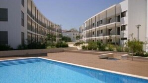 A swimming pool surrounded by modern buildings with balconies, a clear sky, and some greenery. - Duplex apartment in the center of town with swimming pool, 3 bedrooms, for 6 (tavira)
