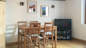 Zona pranzo con tavolo e sedie in legno, televisore e due quadri appesi al muro.