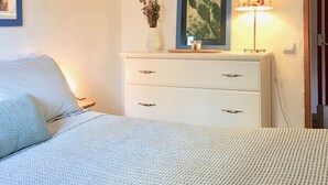 Una camera da letto con un letto, una cassettiera, una lampada e una finestra con persiane.