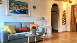 Un soggiorno con un divano blu, un cactus su un tavolino e un quadro che raffigura una cittadina costiera.