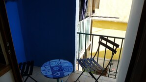 Un piccolo balcone con un tavolo e due sedie piastrellati di blu, una parete gialla e una ringhiera metallica.