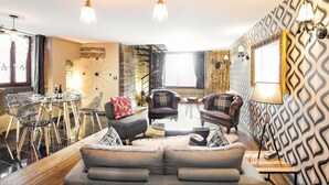 A modern living room with a sofa, chairs, a dining table, and a staircase. - Charming Gite in Medieval Village 1mn walk to Shops & Restaurants (Nolay)