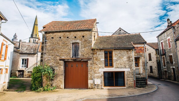 A stone building with a brown wooden door and windows, surrounded by a narrow street and other buildings. - Charming Gite in Medieval Village 1mn walk to Shops & Restaurants (Nolay)