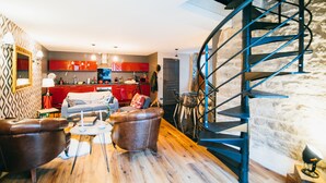 A modern living room with a wooden floor, leather armchairs, a coffee table, and a red kitchen in the background. - Charming Gite in Medieval Village 1mn walk to Shops & Restaurants (Nolay)