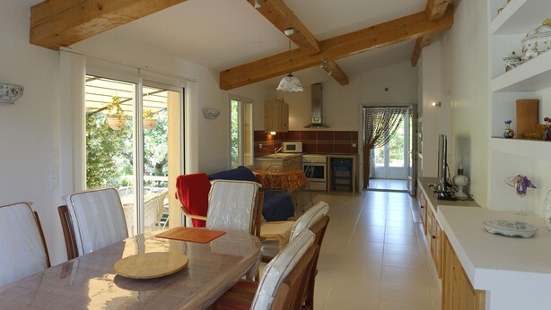 A spacious kitchen with wooden beams, a dining area with a large table and chairs, and a view through the glass doors. -  part of villa on the ground floor next to a vineyard (Lorgues)